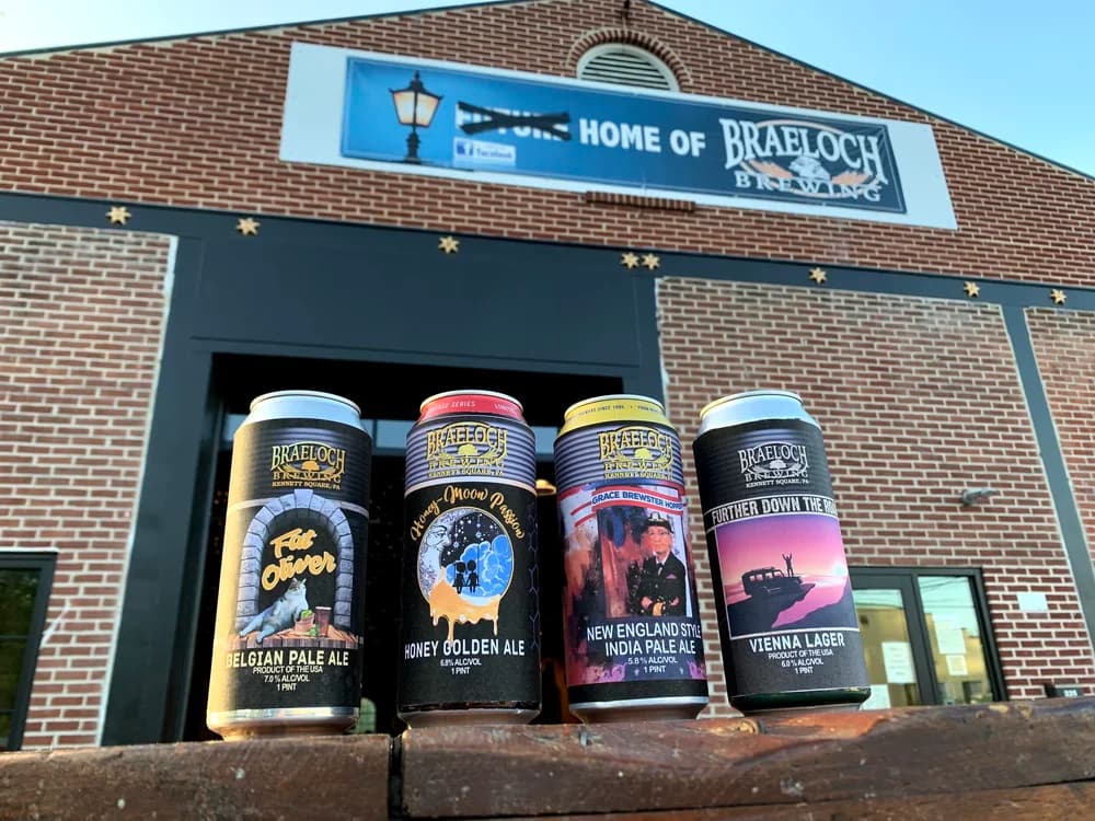 Four Braeloch cans lined up in front of the brick brewery